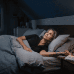 A woman lying wide awake in bed at midnight experiencing high nighttime cortisol symptoms and insomnia.